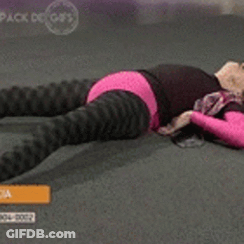 A Woman In A Pink Top And Black Pants Is Laying On The Floor Stretching Her Legs GIF