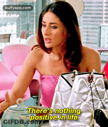 A Woman In A Pink Top Is Sitting At A Table With Handbags And Says `` There 'S Nothing Positive In Life '' . GIF