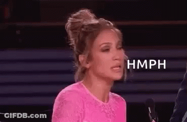 A Woman In A Pink Top Is Sitting In Front Of A Microphone And Making A Funny Face . GIF
