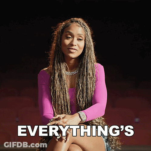 A Woman In A Pink Top Is Sitting With Her Legs Crossed And The Words Everything 'S Behind Her GIF