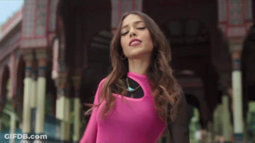 A Woman In A Pink Top Is Standing In Front Of A Building With Her Eyes Closed GIF