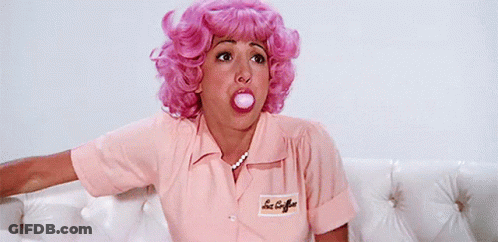 A Woman In A Pink Wig Blowing A Bubble With Her Mouth GIF