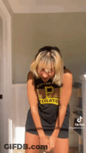 A Woman In A Pittsburgh Pirates Shirt Is Standing In A Room With Her Hands On Her Knees . GIF