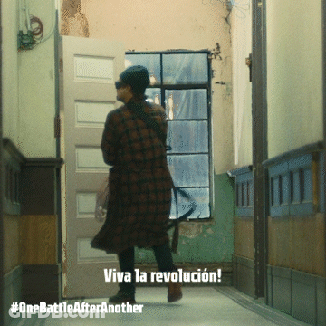 A Woman In A Plaid Coat Is Walking Down A Hallway With The Words Viva La Revolucion On The Bottom GIF