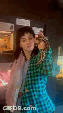 A Woman In A Plaid Jacket Is Holding A Snake Over Her Head . GIF