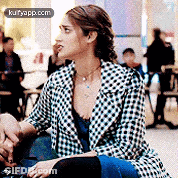 A Woman In A Plaid Jacket Is Sitting At A Table In A Cafe . GIF
