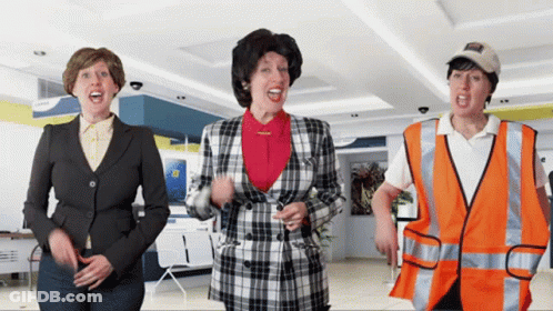 A Woman In A Plaid Jacket Stands Next To Two Other Women GIF