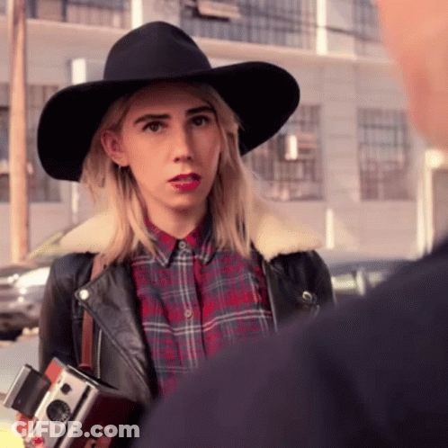 A Woman In A Plaid Shirt And A Black Hat Holds A Camera GIF
