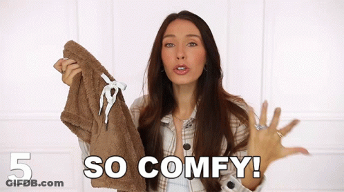 A Woman In A Plaid Shirt Is Holding A Brown Jacket And Saying So Comfy GIF