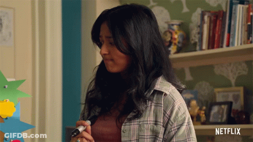 A Woman In A Plaid Shirt Is Holding A Marker In Front Of A Shelf With Netflix Written On It GIF