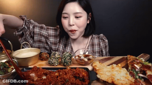 A Woman In A Plaid Shirt Is Sitting At A Table Eating Food . GIF