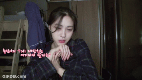 A Woman In A Plaid Shirt Is Sitting In A Room With Korean Writing On The Walls GIF