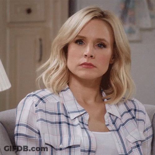 A Woman In A Plaid Shirt Is Sitting On A Couch Looking At The Camera GIF