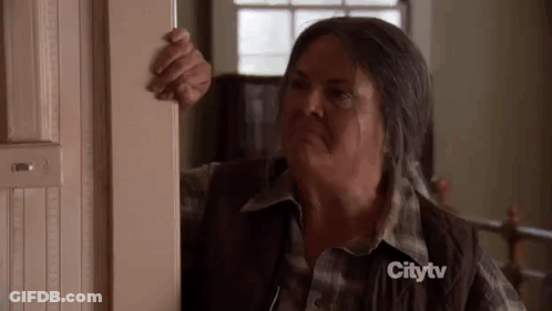 A Woman In A Plaid Shirt Is Standing In A Doorway And Looking Out . GIF