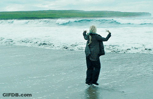 A Woman In A Plaid Shirt Is Standing On A Beach GIF
