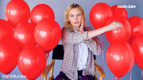 A Woman In A Plaid Shirt Is Surrounded By Red Balloons With Marie Claire Written In The Corner GIF