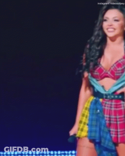 A Woman In A Plaid Top And Skirt Is Standing On A Stage . GIF