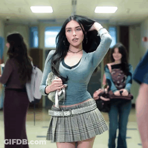 A Woman In A Pleated Skirt Holds Her Hair In A Hallway GIF