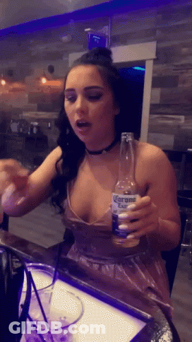 A Woman In A Plunging Neckline Holds A Bottle Of Corona GIF