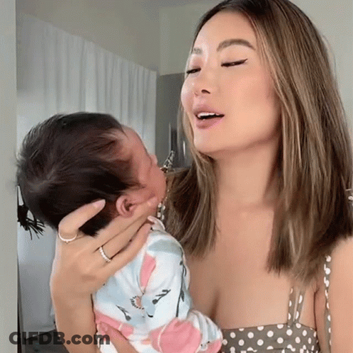 A Woman In A Polka Dot Dress Holds A Baby GIF