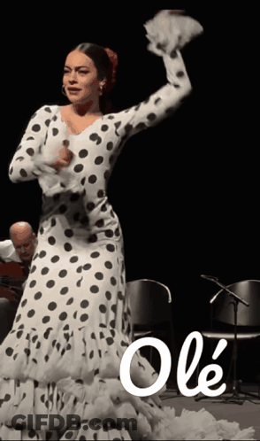 A Woman In A Polka Dot Dress Is Dancing In Front Of A Man Playing Guitar GIF