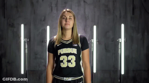 A Woman In A Purdue Jersey Stands In Front Of A Row Of Lights GIF
