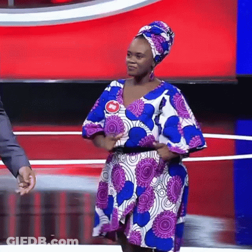 A Woman In A Purple And Blue Dress Is Standing On A Stage With A Man Holding Her Hand . GIF