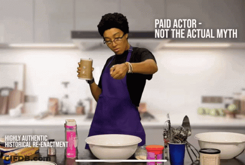 A Woman In A Purple Apron Is Holding A Cup Of Coffee In A Kitchen GIF