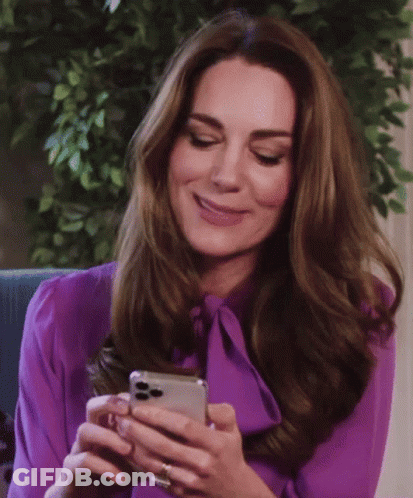 A Woman In A Purple Blouse Is Smiling While Looking At Her Phone GIF