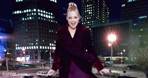 A Woman In A Purple Coat Is Dancing In Front Of A City At Night GIF