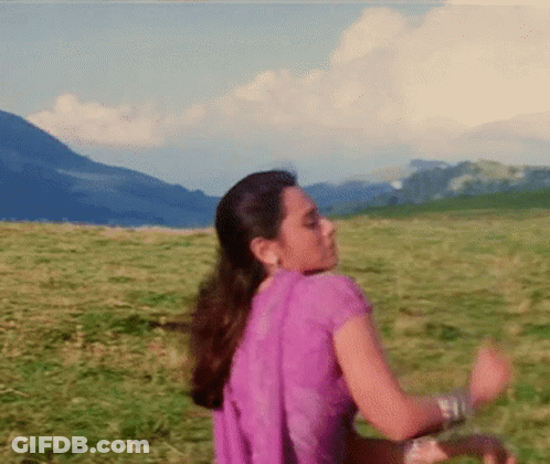 A Woman In A Purple Dress Is Dancing In A Grassy Field With Mountains In The Background . GIF