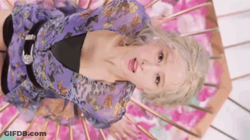 A Woman In A Purple Dress Is Laying On Her Stomach On A Pink Surface . GIF