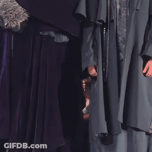 A Woman In A Purple Dress Is Peeking Out From Behind A Purple Cloth GIF