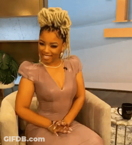 A Woman In A Purple Dress Is Sitting In A Chair And Smiling GIF
