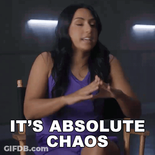 A Woman In A Purple Dress Is Sitting In A Director 'S Chair And Saying It 'S Absolute Chaos GIF