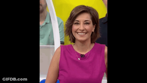 A Woman In A Purple Dress Is Smiling In Front Of A Yellow Wall . GIF