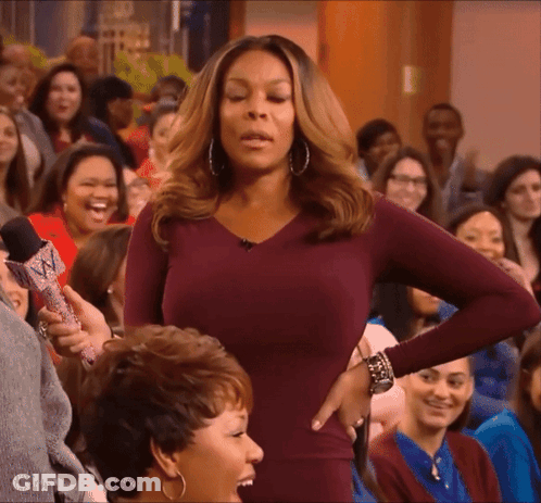 A Woman In A Purple Dress Is Standing In Front Of A Crowd Holding A Microphone GIF
