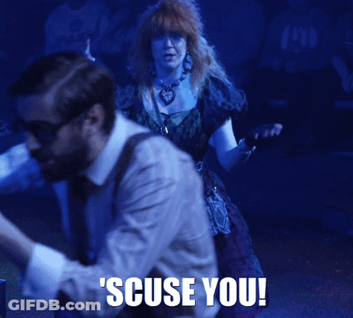 A Woman In A Purple Dress Is Standing In Front Of A Man With The Words Scuse You Written On The Bottom GIF
