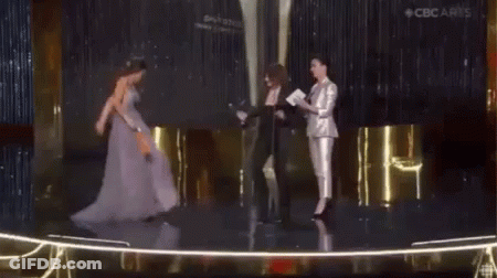 A Woman In A Purple Dress Is Standing On A Stage Holding A Trophy . GIF