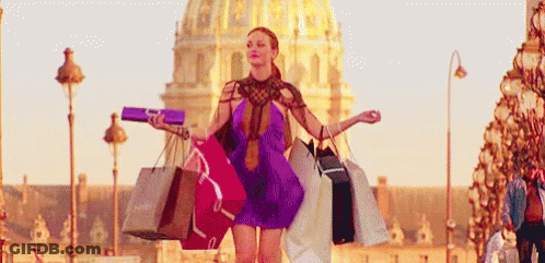 A Woman In A Purple Dress Is Walking Down A Street Holding Shopping Bags . GIF