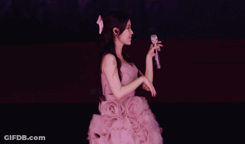 A Woman In A Purple Dress Sings Into A Microphone GIF