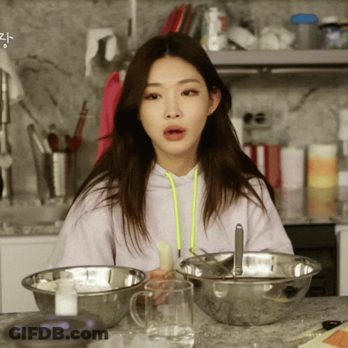 A Woman In A Purple Hoodie Sits At A Counter With Bowls Of Food And A Glass Of Water GIF