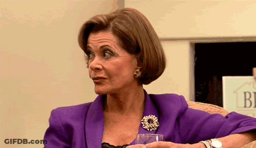 A Woman In A Purple Jacket Is Sitting On A Couch Holding A Glass Of Wine . GIF