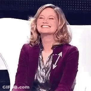 A Woman In A Purple Jacket Is Smiling And Sitting On A White Chair . GIF