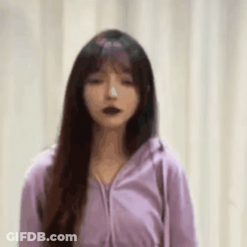 A Woman In A Purple Jacket Is Standing In Front Of A White Curtain . GIF