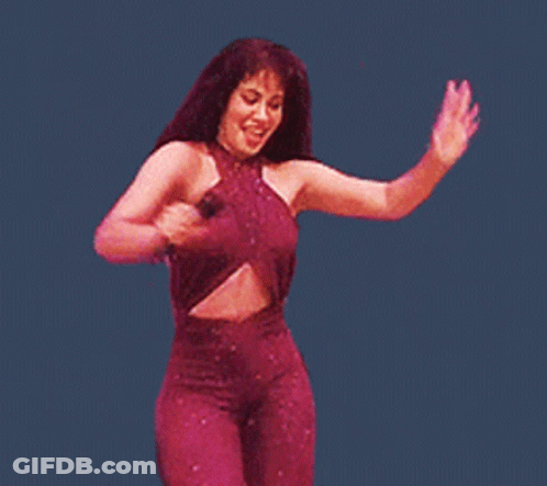 A Woman In A Purple Jumpsuit Is Holding A Microphone And Dancing GIF