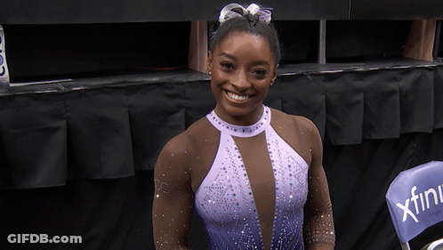 A Woman In A Purple Leotard Is Smiling In Front Of A Chair That Says Xfinity GIF