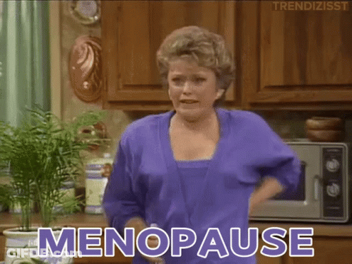 A Woman In A Purple Robe Is Standing In A Kitchen And Says " Menopause " GIF