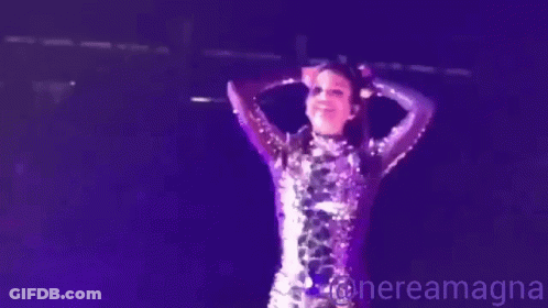 A Woman In A Purple Sequined Dress Is Standing On A Stage In Front Of A Microphone .. GIF