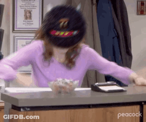 A Woman In A Purple Shirt And A Black Hat Is Sitting At A Desk . GIF
